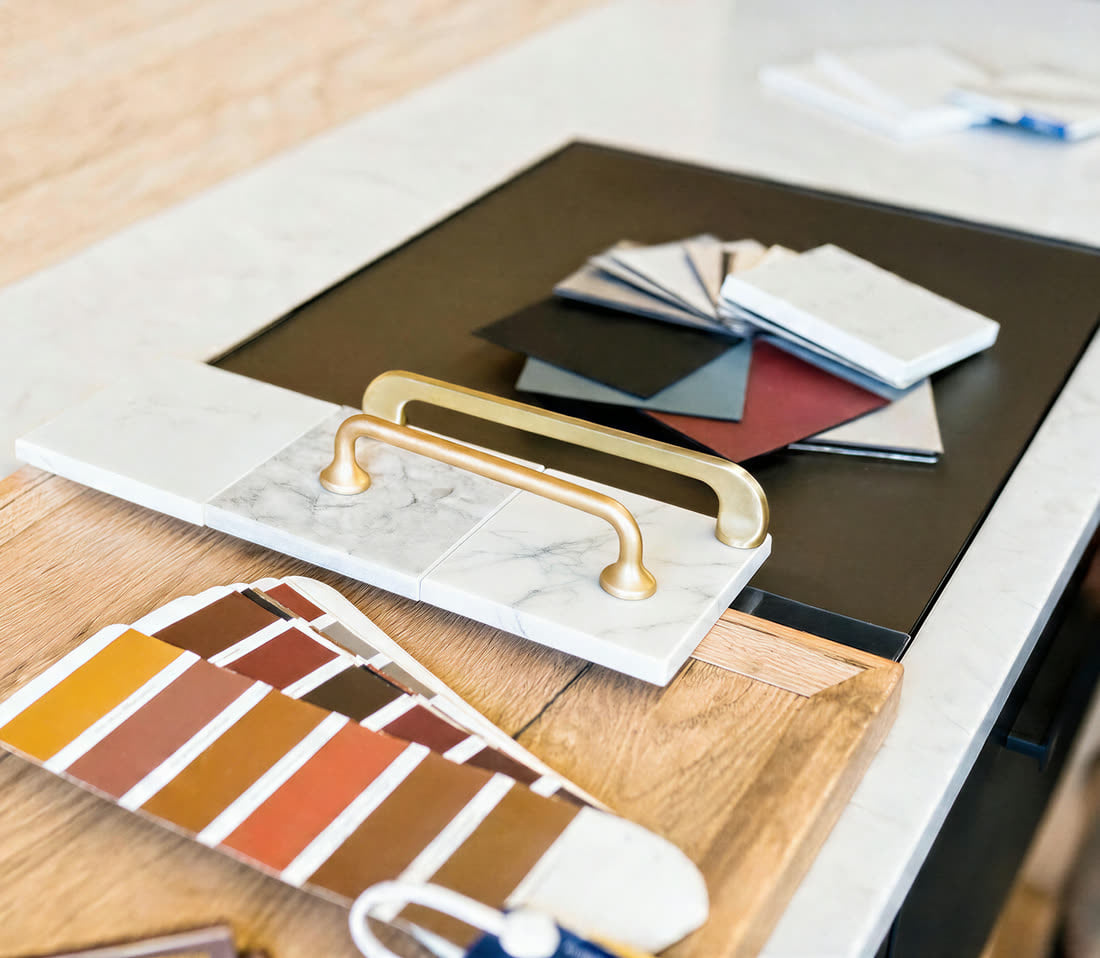 Brass cabinet pull, marble sample and finish swatches laid out on a countertop