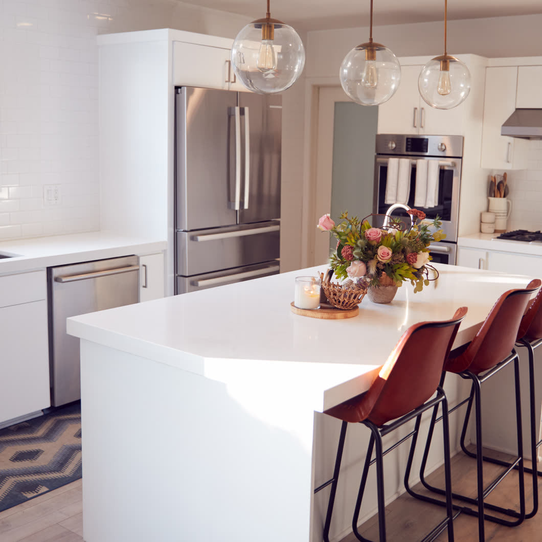 Bright kitchen with a white waterfall island, pendant lights and leather stools