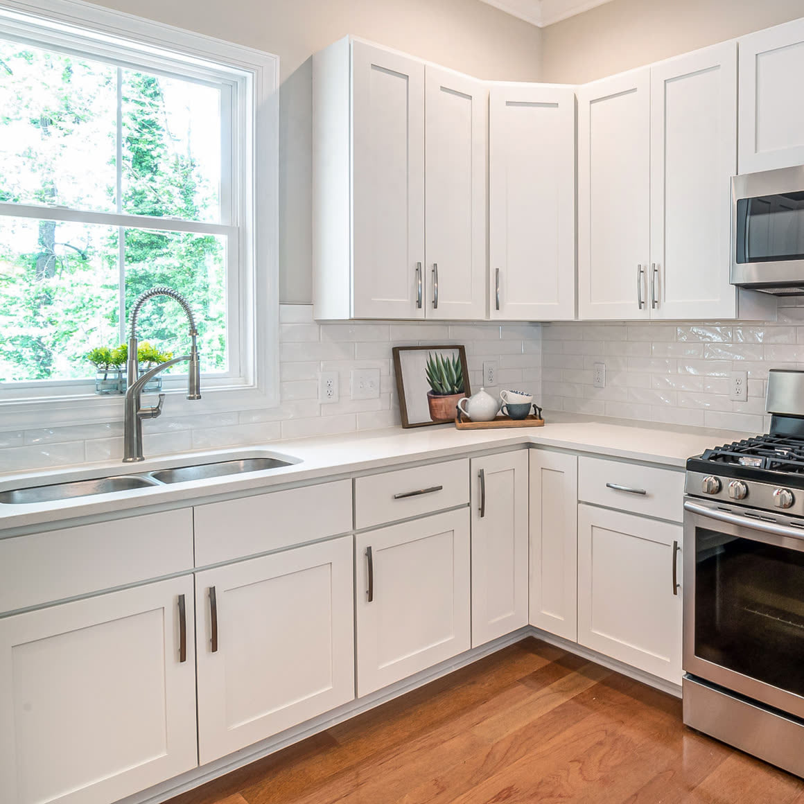 Bright white kitchen with shaker cabinets, a window over the sink and a gas range